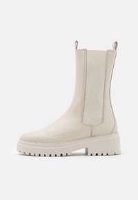 Beige ankle boots made of leather with elastic side panels, a chunky white sole, and pull loops on the back for easy wear.