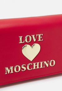 Punainen tekonahkainen lompakko, jossa on kultasävyinen kohokuvioitu "LOVE" -teksti ja sydämen muotoilua, sekä "MOSCHINO" näyttävän kultakirjaimin.