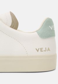 Hvit lær sneaker med teksturert finish, lysegrønn semsket hælflik og preget merkevare i gull på siden. Glatt gummisåle.