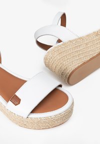 Sandalias espadrilles blancas con una plataforma de yute trenzado y plantilla en tono marrón. Presentan correas anchas, una textura suave y un pequeño acento de marca.