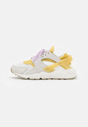 Baskets de sport avec mesh blanc, superpositions jaune pâle et lacets violet clair, présentées sur un fond blanc.