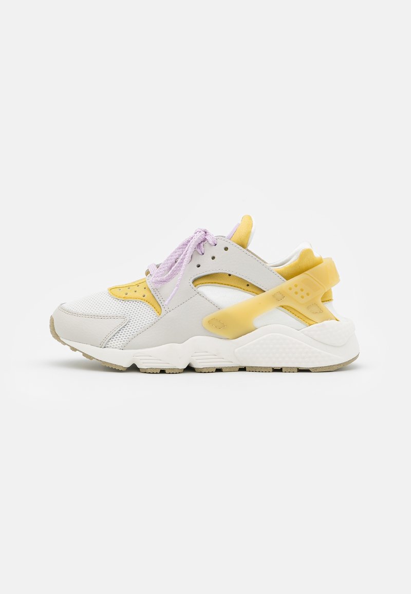 Baskets de sport avec mesh blanc, superpositions jaune pâle et lacets violet clair, présentées sur un fond blanc.