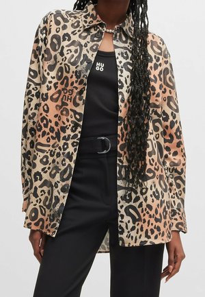 Osoba ubrana w beżową i brązową koszulę na guziki w panterkę, na czarnym topie Hugo, w połączeniu z czarnymi spodniami i czarnym paskiem.