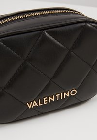 Borsa cosmetica in pelle nera con design trapuntato, hardware dorato e logo "VALENTINO" impresso sul davanti. Chiusura con zip.