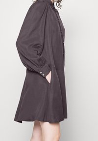Vestito grigio scuro in tessuto morbido, con parte anteriore con bottoni, maniche lunghe a palloncino e tasche sui lati, dalla forma leggermente svasata.