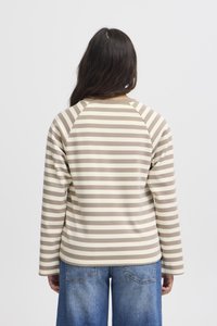 Striped long-sleeve shirt in beige and light brown, featuring a raglan sleeve design and soft texture, paired with blue denim jeans.