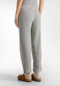Grijze wolmix sweatpants met een relaxed fit, elastische taille en een logo etikett aan de achterkant. Gecombineerd met bruin instapschoenen en beige sokken.