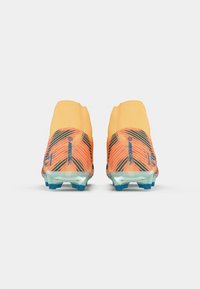 Een paar oranje en zwarte gestreepte voetbalschoenen met blauwe noppen, getoond vanaf de achterkant op een witte achtergrond.
