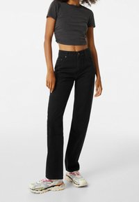 Jeans negros de cintura alta con un corte recto, combinados con una camiseta negra corta. El conjunto se completa con zapatillas multicolores.