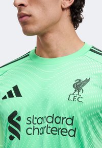 Mann trägt ein hellgrünes Liverpool FC Fußballtrikot mit schwarzen Logos und dem Schriftzug „standard chartered“ als Sponsor.