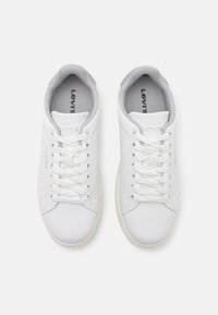 Białe sneakersy z gładkiego materiału syntetycznego, sznurowanym designem, wyściełanymi kołnierzami oraz szarymi akcentami wewnątrz i na pięcie. Widoczny mały detal logo.