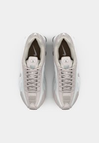 Baskets de sport gris clair avec une tige en maille et cuir, dotées d'un embout texturé, de lacets et d'une semelle intermédiaire blanche avec des accents foncés.