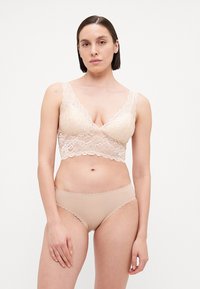 Lace bralette with a V-neck, scalloped edges, and sheer design; paired with seamless bikini in a matching nude tone.
