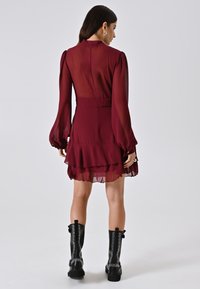 Burgunder Kleid mit langen, durchsichtigen Ärmeln, hohem Kragen und geschichtetem Volant-Saum. Kombiniert mit schwarzen, mit Nieten versehenen Combat Boots.
