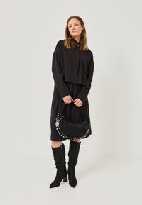 Black cropped top, matching black dress, knee-high black suede boots, and a black bag with silver studs and a chain detail.