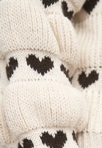 Krémsvětlá pletenina s vzorem rovnoměrně rozložených černých srdcí, zobrazující texturu hrubého stehu a záhyby.