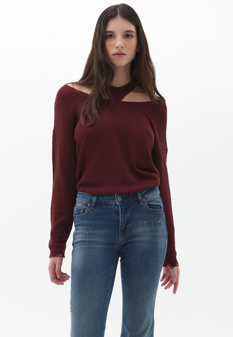 Maglione bordeaux con design a spalla aperta, texture a maglia e maniche lunghe, abbinato a jeans blu strappati. Stile semplice e moderno.