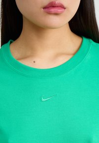 Zaļa kokvilnas T-kreklu ar apļa kakla izgriezumu, ar mazu izšūtu Nike logo nedaudz tumšākā zaļā krāsā. Gluda tekstūra un pieguļoša forma.