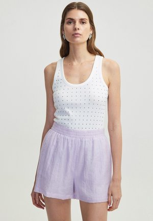 Débardeur blanc avec des clous noirs, associé à un short violet clair avec une taille élastique et un tissu texturé.