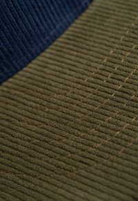 Two textured fabric sections: one navy ribbed and one olive green with fine horizontal lines and subtle stitching details.