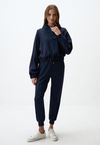 Tuta blu navy con pullover a zip a quarto e pantaloni con cordino, caratterizzato da polsini elasticizzati e una vestibilità comoda, realizzato in tessuto morbido.