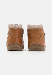 Bottes chelsea en cuir marron avec col en polaire beige doux, semelles texturées et coutures contrastées. Présente une étiquette de marque embossée sur la semelle.