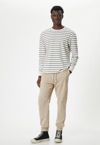 Långärmad randig skjorta i vitt och marinblått, kombinerad med beige joggerbyxor med elastiska muddar och svarta hög-topp sneakers.
