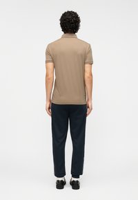 Ανδρικό πόλο μπλουζάκι σε ανοιχτό καφέ χρώμα με κοντά μανίκια, σε συνδυασμό με μπλε σκούρο παντελόνι φόρμας με ρίγες στα πλάγια, από την πίσω πλευρά.