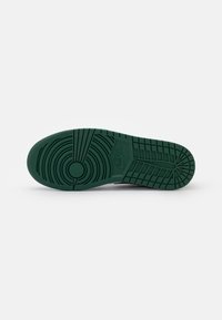 Nike-kengän pohja, jossa on teksturoitu vihreä kumimateriaali, pyöreillä ja lineaarisilla urilla, tuotemerkin logo ja korostetut pito-ominaisuudet.