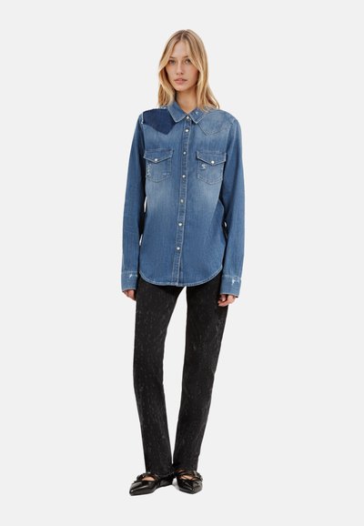 Camisa de mezclilla con un acabado azul desgastado, dos bolsillos frontales, cierre de botones y mangas largas, combinada con pantalones negros con estampado y ballerinas negras.