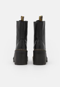 Pair of black leather boots with chunky ribbed heels, yellow stitching, and black-and-yellow pull tabs, shown from the back on white background.