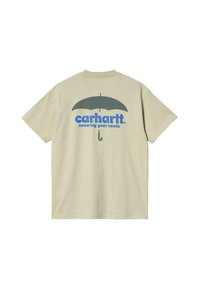 Camiseta de algodón color beige claro con un gráfico azul de un paraguas y el texto "Carhartt cubriendo tus necesidades" debajo. Manga corta, ajuste casual.