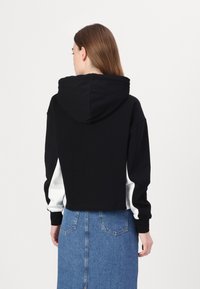 Hanorac scurt, negru, cu glugă gri, având accente albe pe mâneci. Textură fină, design sportiv și buzunar tip cangur.