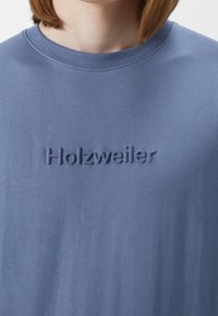 T-shirt in cotone blu con scollatura rotonda e logo "Holzweiler" ricamato al centro. Tessuto liscio.