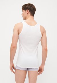 Bijela pamučna majica bez rukava s uskim dizajnom, sa širokim naramenicama i zaobljenim izrezom, uparena s svijetlosivim šortsem.