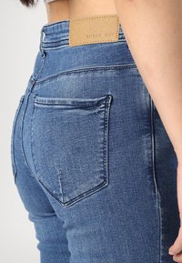 Mörkblå denimjeans med högmidjad design, med en läderetikett på midjan och två bakfickor.