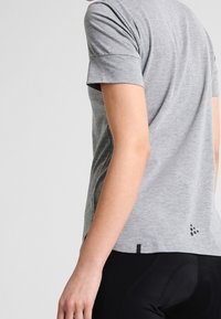 Camiseta deportiva gris de manga corta y ajuste ligeramente holgado, con detalles reflectantes en la parte trasera y una textura suave.
