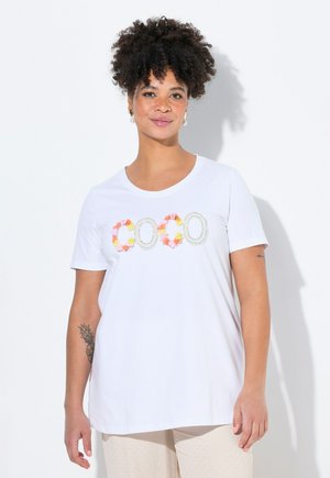 T-shirt blanc à manches courtes avec col rond, présentant des lettres en appliqué floral coloré épelant "COCO" sur le devant. Tissu en coton doux.