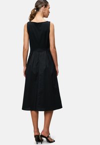 Black sleeveless dress with a fitted bodice, flared skirt, and back zipper. Smooth texture with minimal accents and knee-length hem.