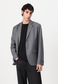 Gray pinstriped blazer with notch lapels, single-button closure, and front pockets, worn over a black t-shirt and dark jeans.