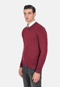 Maglione a maglia color bordeaux con scollo rotondo e maniche lunghe. Presenta polsini e orlo a coste. Abbinato a jeans in denim scuri.