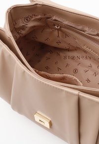 Beige handväska med en slät yta, guldhårdvara och ett fodrat inre med ett upprepat logomönster.