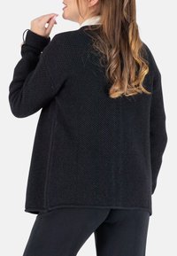 Schwarze Strickjacke mit strukturiertem Design, lockerer Passform und kontrastierendem weißen Kragen. Lange Ärmel mit Manschettendetails.