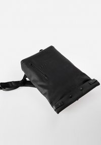 Zaino in pelle nera con spallacci regolabili, tasca frontale con zip, texture liscia e dettagli abbottonati nella parte inferiore. Design minimalista.