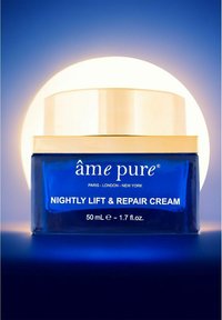 Blå glasburk med ett vitt och guldlock, märkt "âme pure Nightly Lift & Repair Cream," kapacitet på 50 mL. Belyst bakgrund.