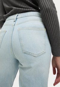 Jeans in denim blu chiaro con una vestibilità aderente, dotati di tasche posteriori e dettagli di cucitura sottili. Il tessuto appare morbido e liscio.