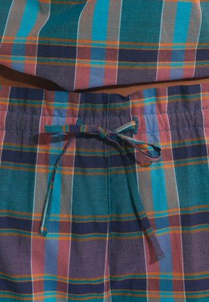 Gros plan sur un tissu à carreaux bleu, sarcelle, violet et orange avec un cordon noué à la taille d’un pantalon léger.