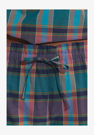 Gros plan sur un tissu à carreaux bleu, sarcelle, violet et orange avec un cordon noué à la taille d’un pantalon léger.