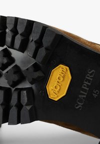 Sort gummisål med dybe riller, featuring et gult Vibram-logo og "SCALPERS 45" prentet, parret med en overdel i brunt ruskind.