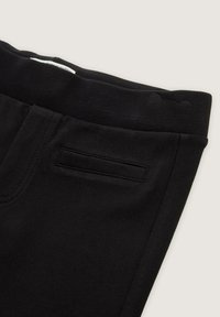 Schwarze Hosen mit elastischem Bund, die eine glatte Oberfläche, eine Seitentasche und saubere Nähte aufweisen. Der Stoff wirkt weich und langlebig.